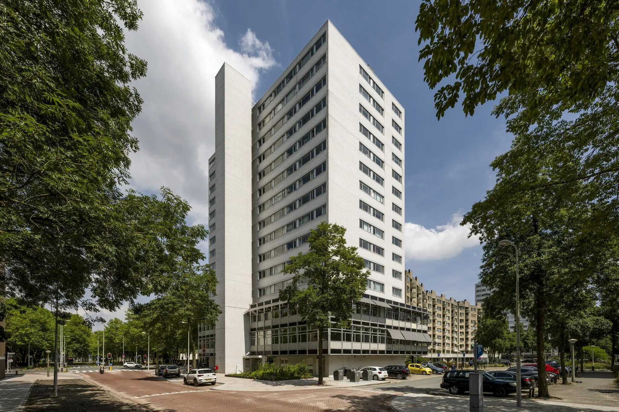 Hoog wit appartementencomplex aan de Van Leijenberghlaan, omgeven door bomen en geparkeerde auto's.